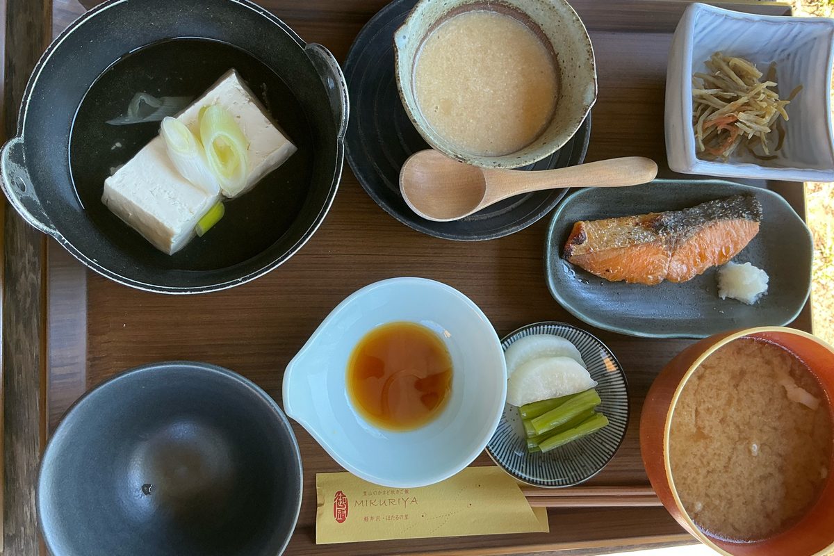 湯豆腐の黒い鍋、焼き鮭、とろろ、きんぴら、漬物、汁物が並んだお盆